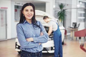 Woman at a car garage getting mechanical service. The mechanic works under the hood of the car photo