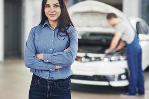 Woman at a car garage getting mechanical service. The mechanic works under the hood of the car photo