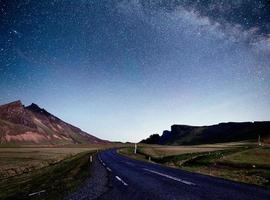 Starry Sky over the mountains. The asphalt road with white markings. Beautiful summer landscape. Soft filtering effect. Iceland photo