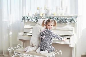 Two happy little girls in pajamas play the piano on Christmas day photo