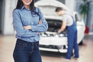 mujer en un garaje de automóviles recibiendo servicio mecánico. el mecánico trabaja bajo el capó del coche foto