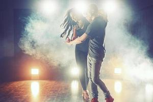 hábiles bailarines actuando en la habitación oscura bajo la luz y el humo del concierto. pareja sensual realizando una danza contemporánea artística y emocional foto