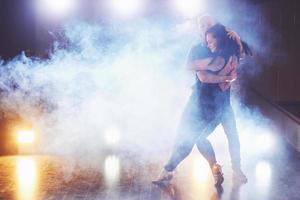 hábiles bailarines actuando en la habitación oscura bajo la luz y el humo del concierto. pareja sensual realizando una danza contemporánea artística y emocional foto