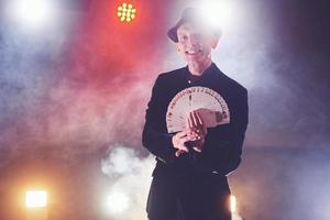 Magician showing trick with playing cards. Magic or dexterity, circus, gambling. Prestidigitator in dark room with fog photo