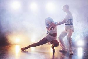 hábiles bailarines actuando en la habitación oscura bajo la luz y el humo del concierto. pareja sensual realizando una danza contemporánea artística y emocional foto