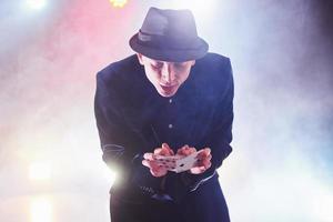 Magician showing trick with playing cards. Magic or dexterity, circus, gambling. Prestidigitator in dark room with fog photo