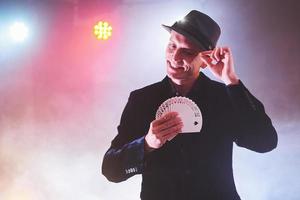 Magician showing trick with playing cards. Magic or dexterity, circus, gambling. Prestidigitator in dark room with fog photo