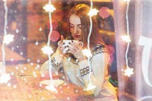 Young beautiful woman sitting in cafe, drinking coffee. Christmas, new year, winter holidays concept double exposure, night city photo
