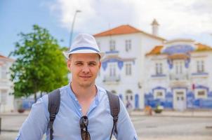 Young man traveler with white hat looking at camera posing and smiling in streets of Aveiro city in Portugal photo