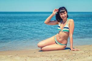 hermosa joven en bikini sentarse en la playa de arena