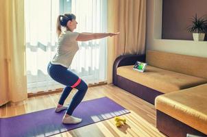 joven mujer atractiva en ropa deportiva haciendo ejercicio en casa, haciendo sentadillas con banda de resistencia de goma foto