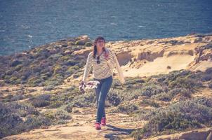 una joven viajera con un cárdigan a rayas mantiene una chaqueta blanca, sonríe y camina por los acantilados costeros de la bahía de dwejra foto