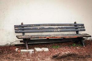 Old gray wooden bench standing on dry grass near plaster wall photo