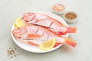 Raw red tilapia fish is a kind of freshwater fish consumption, served on white plate with spices and lemon. Selected focus photo