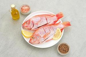 El pescado crudo de tilapia roja es un tipo de consumo de pescado de agua dulce, servido en un plato blanco con especias y limón. foco seleccionado foto