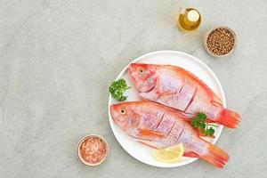 El pescado crudo de tilapia roja es un tipo de consumo de pescado de agua dulce, servido en un plato blanco con especias y limón. foco seleccionado foto