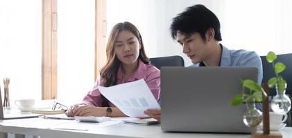 dos alegres jóvenes empresarios asiáticos que trabajan juntos usando una tableta en una oficina moderna. planeando analizar el informe financiero, la inversión del plan de negocios, el concepto de análisis financiero foto