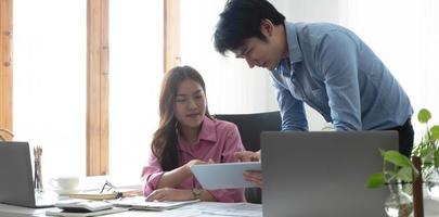 Entrepreneur Asian businessman and businesswoman discussing new business project in tablet in modern Meeting In Modern Office, Asian business casual concept. photo