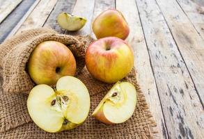 manzanas frescas en saco de arpillera sobre fondo de mesa de madera foto