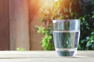 glass of drinking water on wood background and green nature photo
