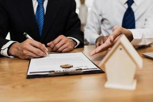 el comprador de la casa firma un contrato en hoja con un agente o corredor en la oficina, concepto como acuerdo de seguro o casa comercial foto