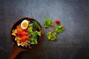 Good health and vegetarian concept, healthy vegetable salad of green fresh vegetable, carrot, corn, and fruit with egg  on plate on dark cement background