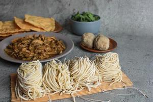 Chicken topping and raw yellow noodle displaying with meatball and green vegetable and fried dumplings photo