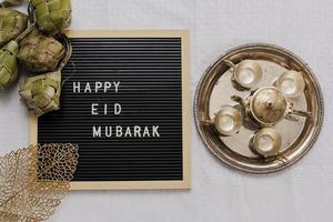 Top view of letter board says Happy Eid Mubarak and traditional food during lebaran celebration called ketupat with set golden teapot and cups photo