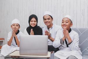 familia musulmana haciendo una conversación en video frente a una computadora portátil con un gesto de saludo manual para el perdón en la celebración de eid mubarak foto