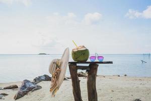 A Coconut fruit and sunglasses with summer hat on wooden table with blurry background of seascape photo
