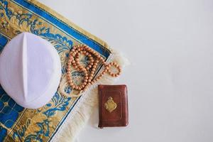 Flat lay of prayer beads and cap on the prayer mat with Holy Book Al Quran. There is Arabic letter which means the holy book photo