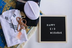 vista superior del vestido tradicional musulmán y cuentas de oración en la alfombra de oración con tablero de letras dice feliz eid mubarak foto