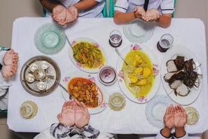 vista superior de las manos familiares rezando antes de comer con el menú servido en la mesa durante eid mubarak foto