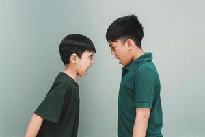 Two angry siblings looking each other and shouting each other on grey background photo