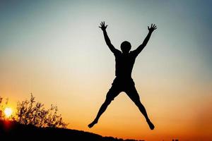 hombre feliz saltando de alegría al atardecer. concepto de éxito y felicidad foto