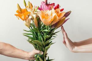 hand gives bouquet of lilies flowers to girl and receives refusal, woman refuses and shows stop sign photo