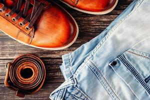 Pair of brown leather male shoes blue jeans and belt dark wooden background, top view closeup photo