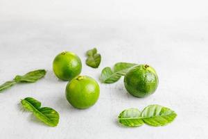 fresh green lime and lime leaves on white wooden table photo