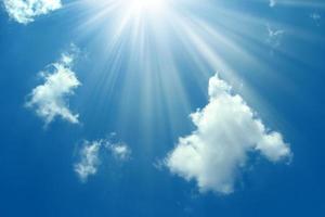 A blue sky with sun and clouds background. Shining sun on blue sky with clouds.Sunny sky background.Blue morning sky, bright sun rising and breaking through the white clouds.The bright midday sun photo