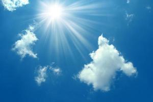 A blue sky with sun and clouds background. Shining sun on blue sky with clouds.Sunny sky background.Blue morning sky, bright sun rising and breaking through the white clouds.The bright midday sun photo
