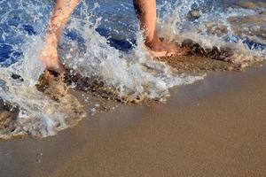 la ola rompe en las piernas de la niña. piernas de una hermosa niña corriendo hacia el océano en una playa de arena. pies femeninos ondeando en la ola del mar. vacaciones en playas paradisíacas. La espuma del mar envuelve la piel de la niña.