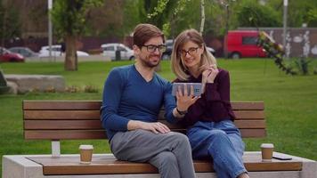 Man And Woman Looking smiling At Phone outdoor sitting on a bench. video