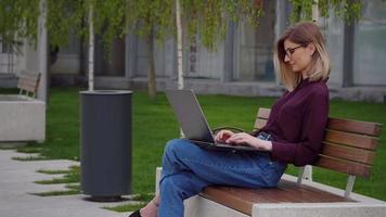 mujer de negocios sentada en un banco al aire libre Park City trabajando en una computadora portátil. video