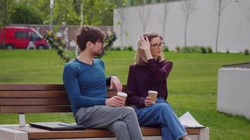 Two friends, pretty woman and handsome man sit on the bench while sipping coffee to-go Coffee Break video