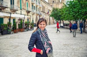 joven hermosa mujer viajera con chaqueta negra mirando a la cámara, sonriendo y posando en el centro histórico de la ciudad de matera foto