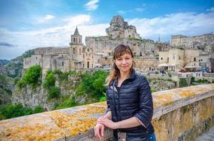 Young beautiful woman traveler with black jacket looking at camera, smile, posing and keep spikelet in Sassi di Matera photo