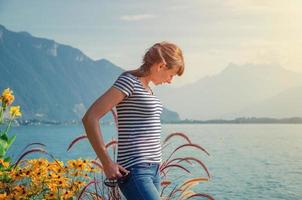 hermosa joven con camisa a rayas y jeans posando y mirando hacia abajo cerca del lago leman ginebra foto