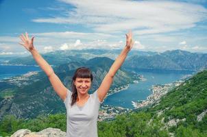 Young beautiful girl traveler with grey t-shirt raise hands and smile on top of mountain photo