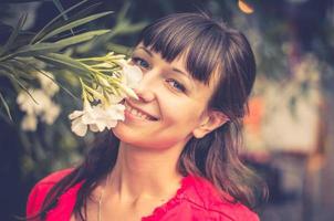 Close-up portrait of young beautiful caucasian girl with red jacket looking at camera, smile and smell white flowers photo