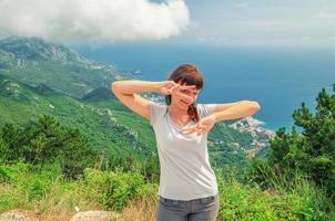 joven hermosa chica viajera con camiseta gris posando y sonriendo en la cima de la montaña foto